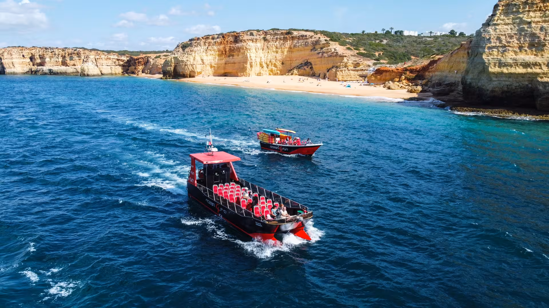 Two tour boats cruising along scenic Algarve golden cliffs and sandy beach near Portimao Portugal