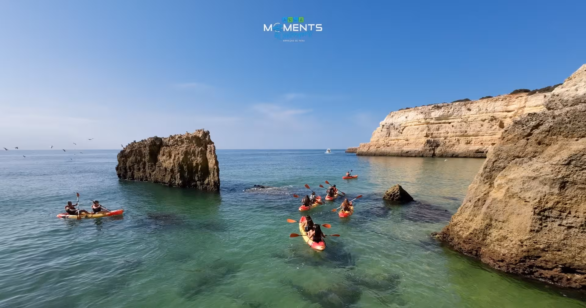 Group of kayakers paddling through turquoise Algarve waters near dramatic golden limestone cliffs and sea stacks