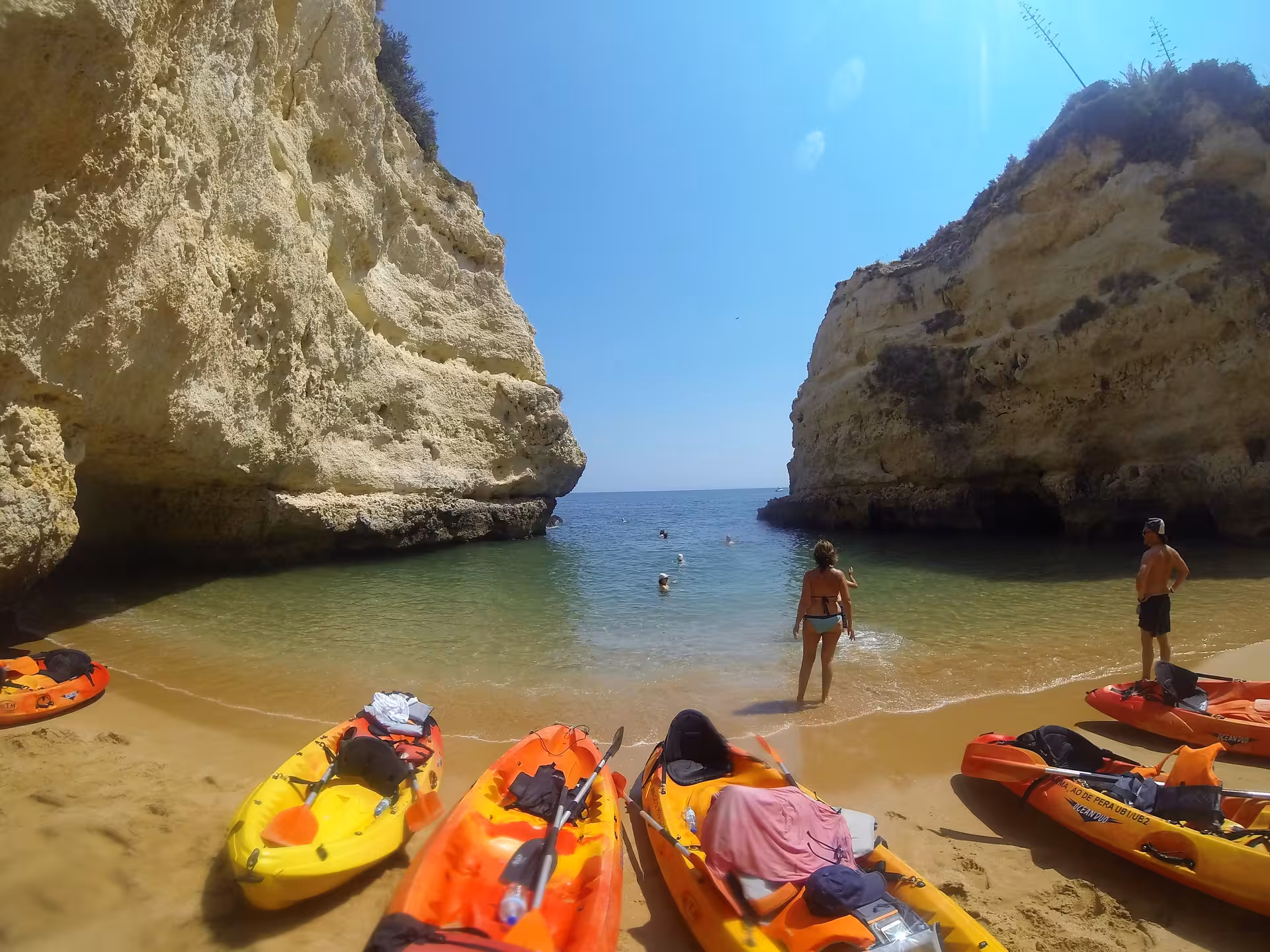 Colorful kayaks resting on a secluded Algarve wild beach surrounded by dramatic golden limestone cliffs and clear water