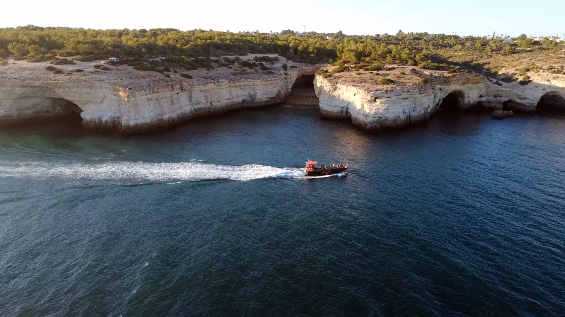 Aerial view of a tour boat cruising past stunning limestone sea caves along the Algarve coast from Portimao