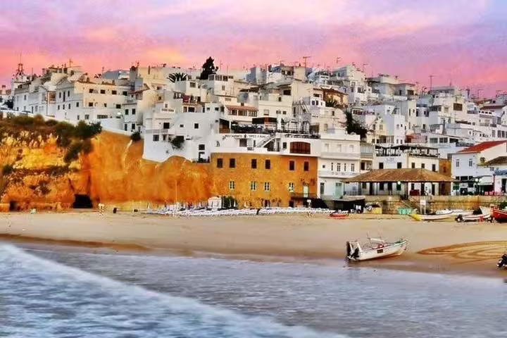Charming Algarve coastal village at sunset, featuring golden cliffs, whitewashed buildings, and boats on sandy beach for private tours.
