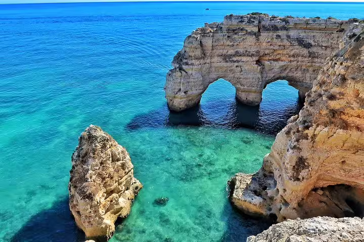 Stunning view of Algarve's rugged coastline with natural rock arches and turquoise waters on a sunny day.