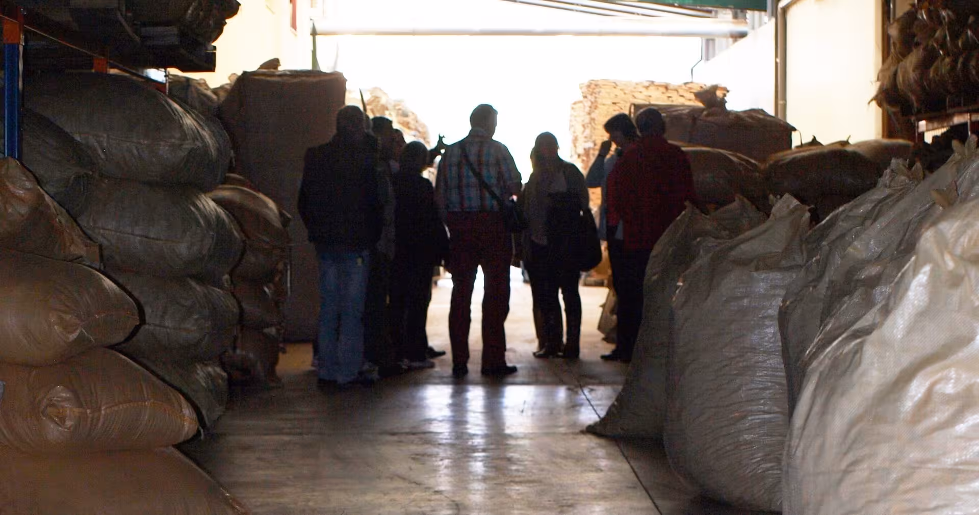 Small tour group exploring an Algarve cork warehouse, walking between giant burlap sacks during a guided visit