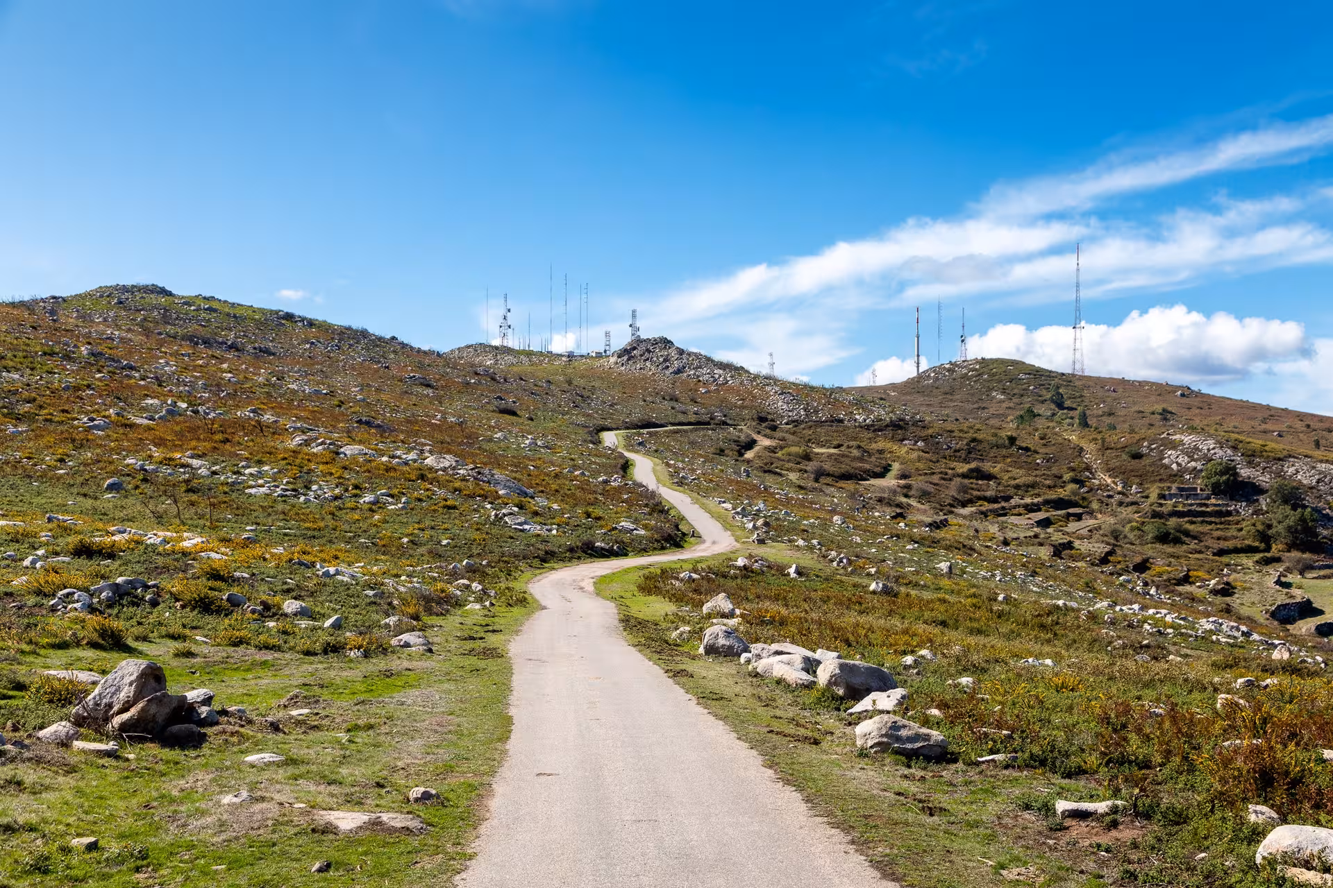 Winding rural road through rocky green hills and radio masts on scenic Algarve à la Carte countryside drive in southern Portugal