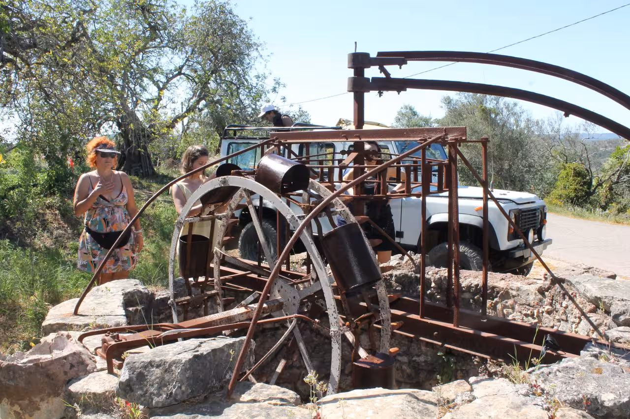 Algarve Grand Safari full-day tour guests viewing an old water wheel by a rural stone well beside a 4x4 jeep