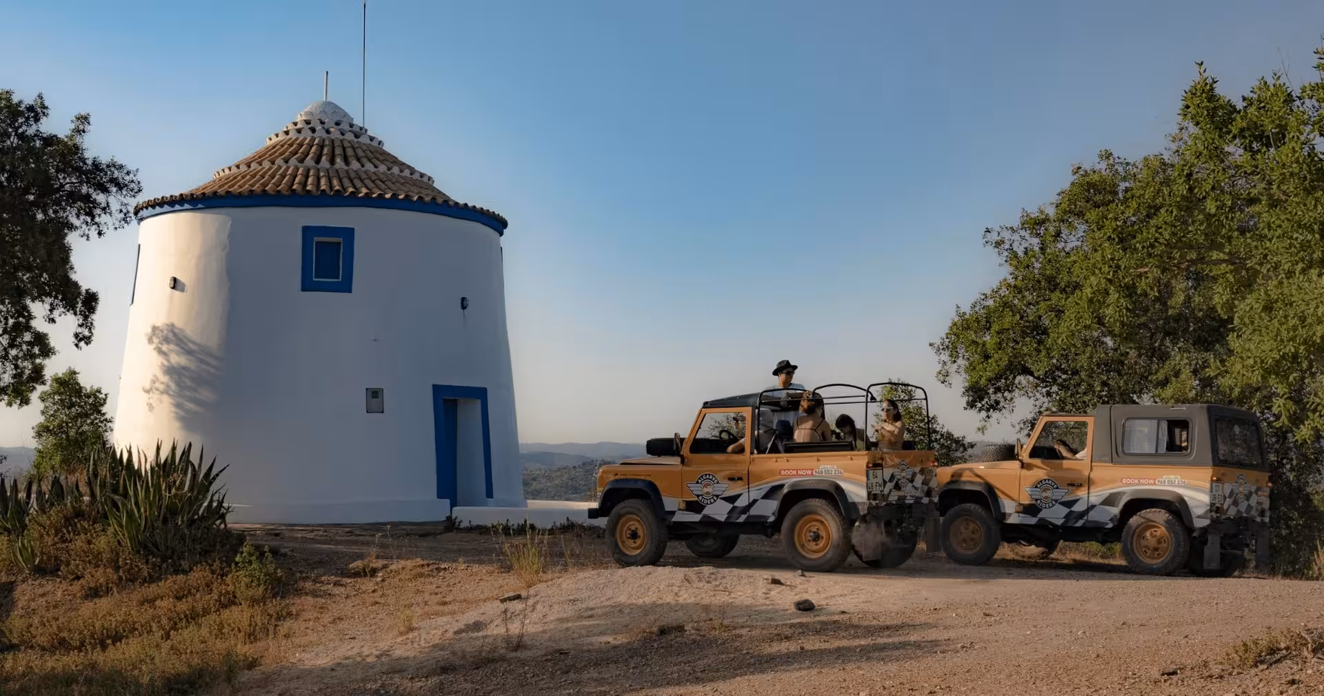 Open-top safari jeeps parked by a traditional white windmill overlooking Algarve hills on The Algarve Heritage Journey