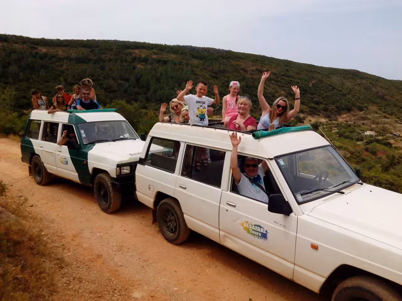 Happy group waving from open-roof jeeps on a dirt track during a full day Algarve countryside jeep safari