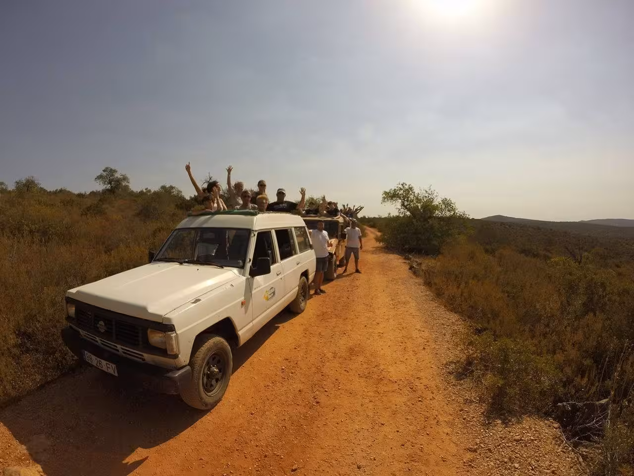 Group enjoying Algarve jeep safari on dusty rural track under sunny sky, part of adventurous half day wine tasting tour