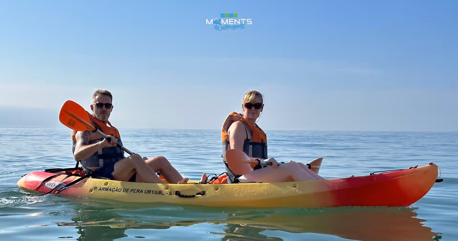 A smiling couple in life jackets paddling a tandem kayak on calm turquoise waters during an Algarve kayak cave tour