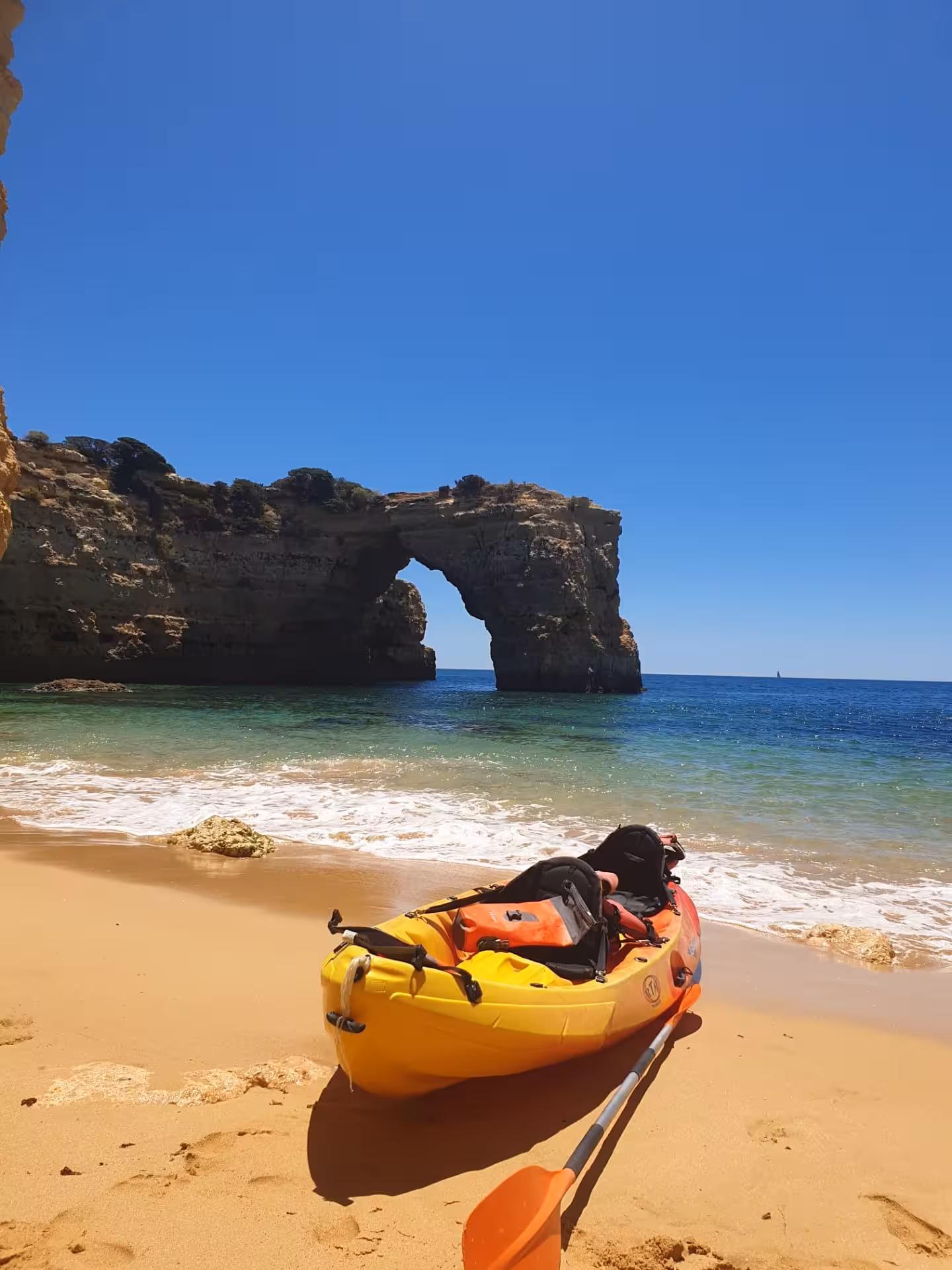 Yellow kayak resting on a wild Algarve beach with a dramatic natural rock arch and turquoise sea backdrop