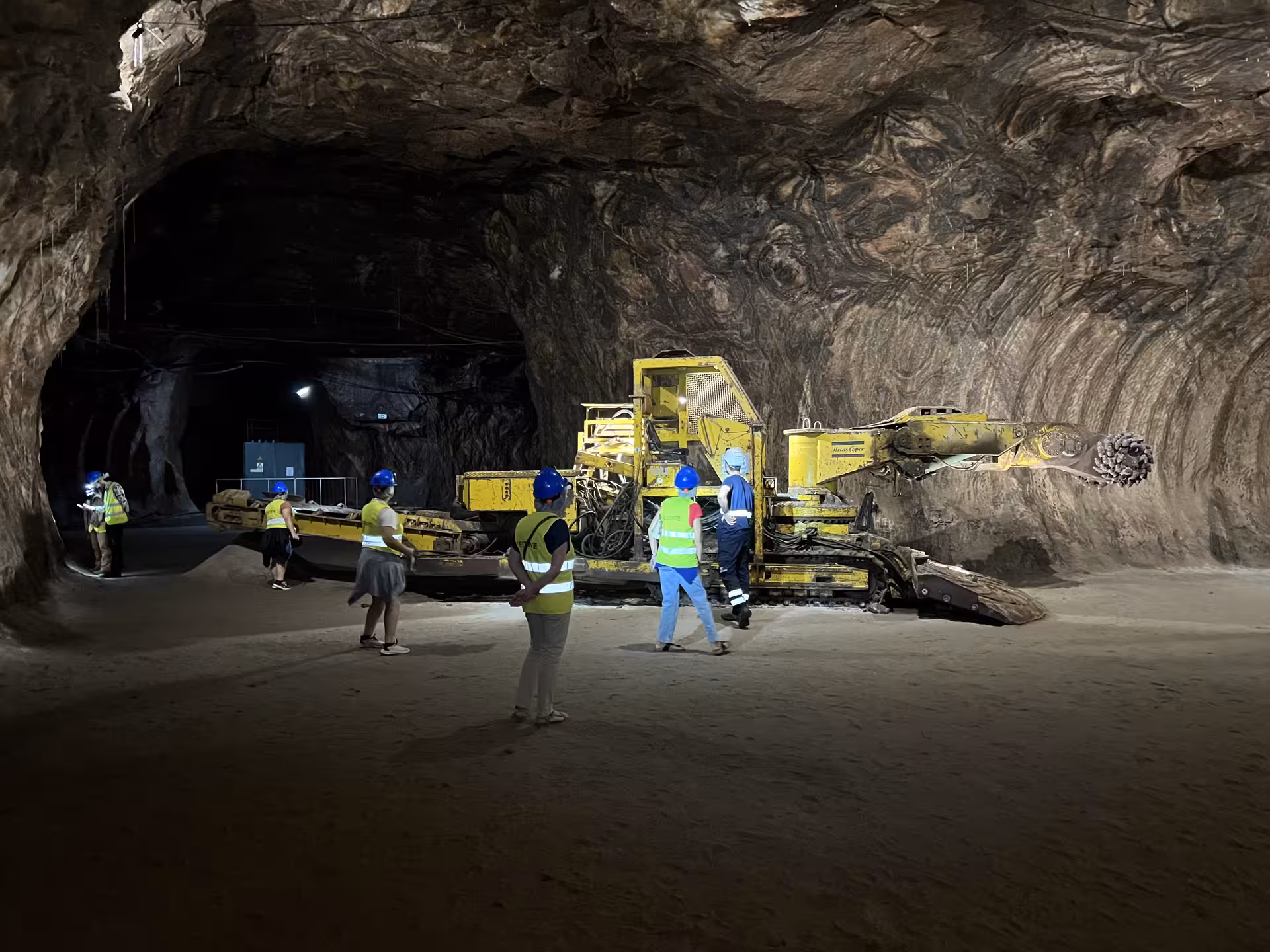 Tourists explore the vast Loulé rocksalt mine, observing mining machinery and geological formations in Algarve.