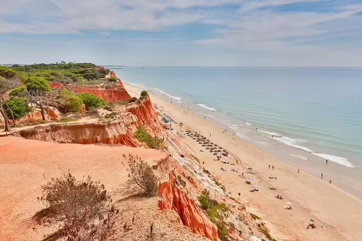 Algarve private tour: stunning red cliffs and pristine beach at Praia da Falésia, Portugal, under a clear blue sky.