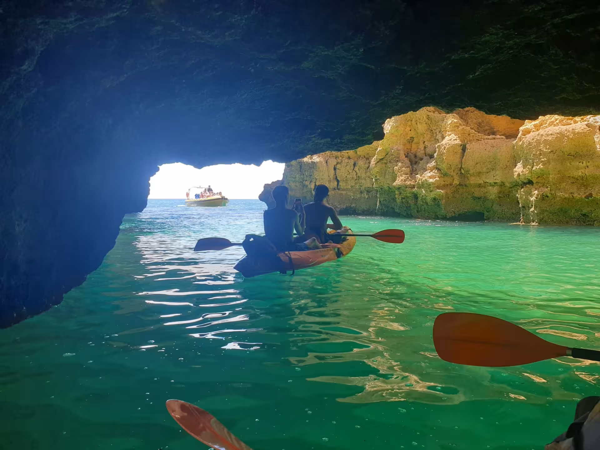 Two kayakers paddling through glowing turquoise waters inside an Algarve sea cave on a guided kayak tour