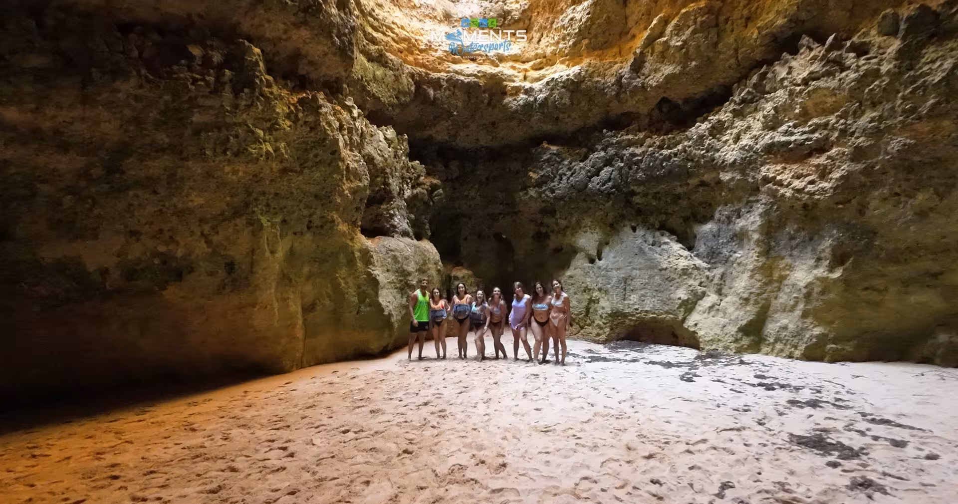 Group of tourists exploring a stunning hidden Algarve sea cave with sandy floor on a kayak adventure tour