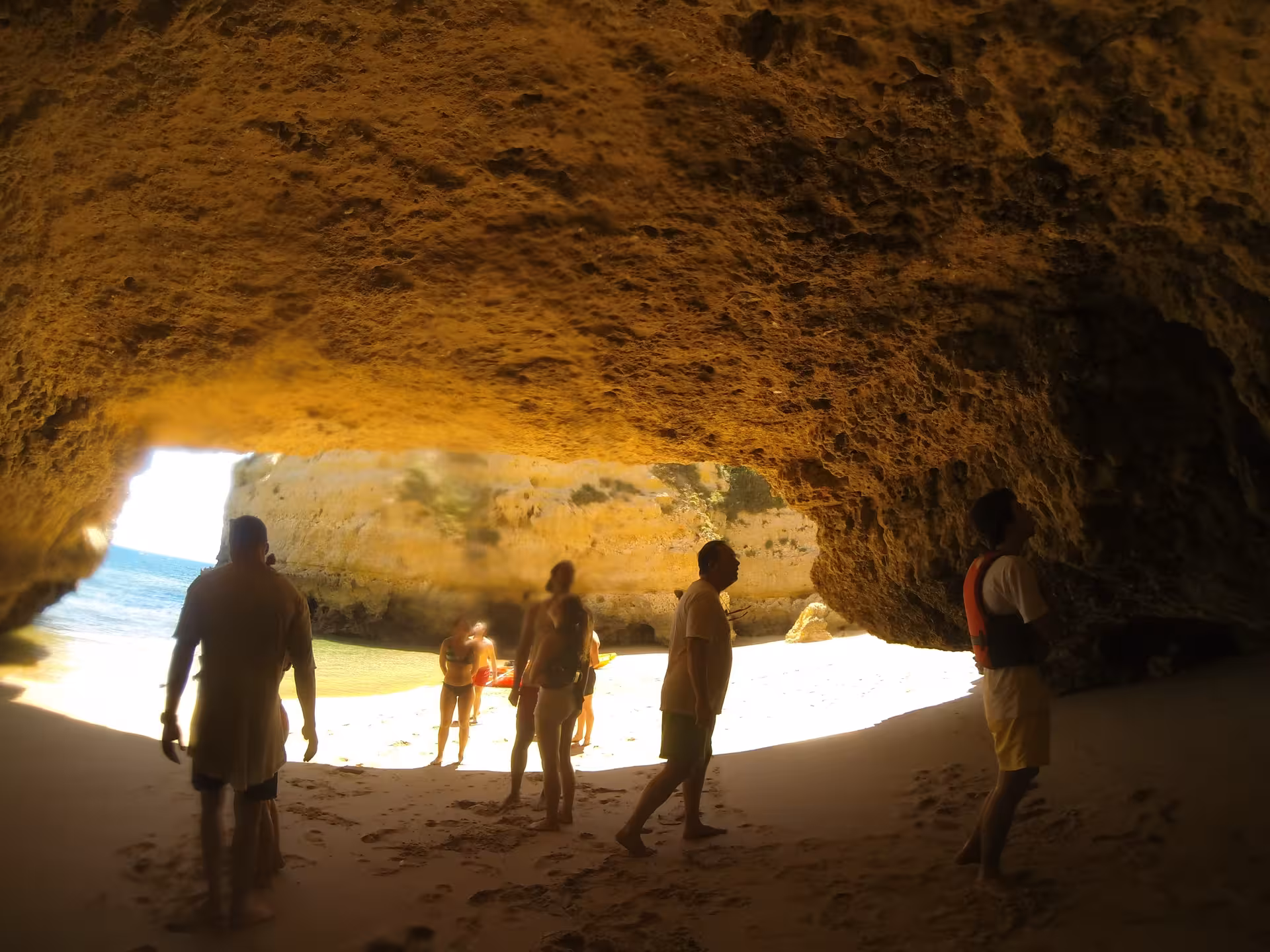 Tourists exploring a stunning Algarve sea cave on a guided kayak tour with sandy beach and turquoise ocean views