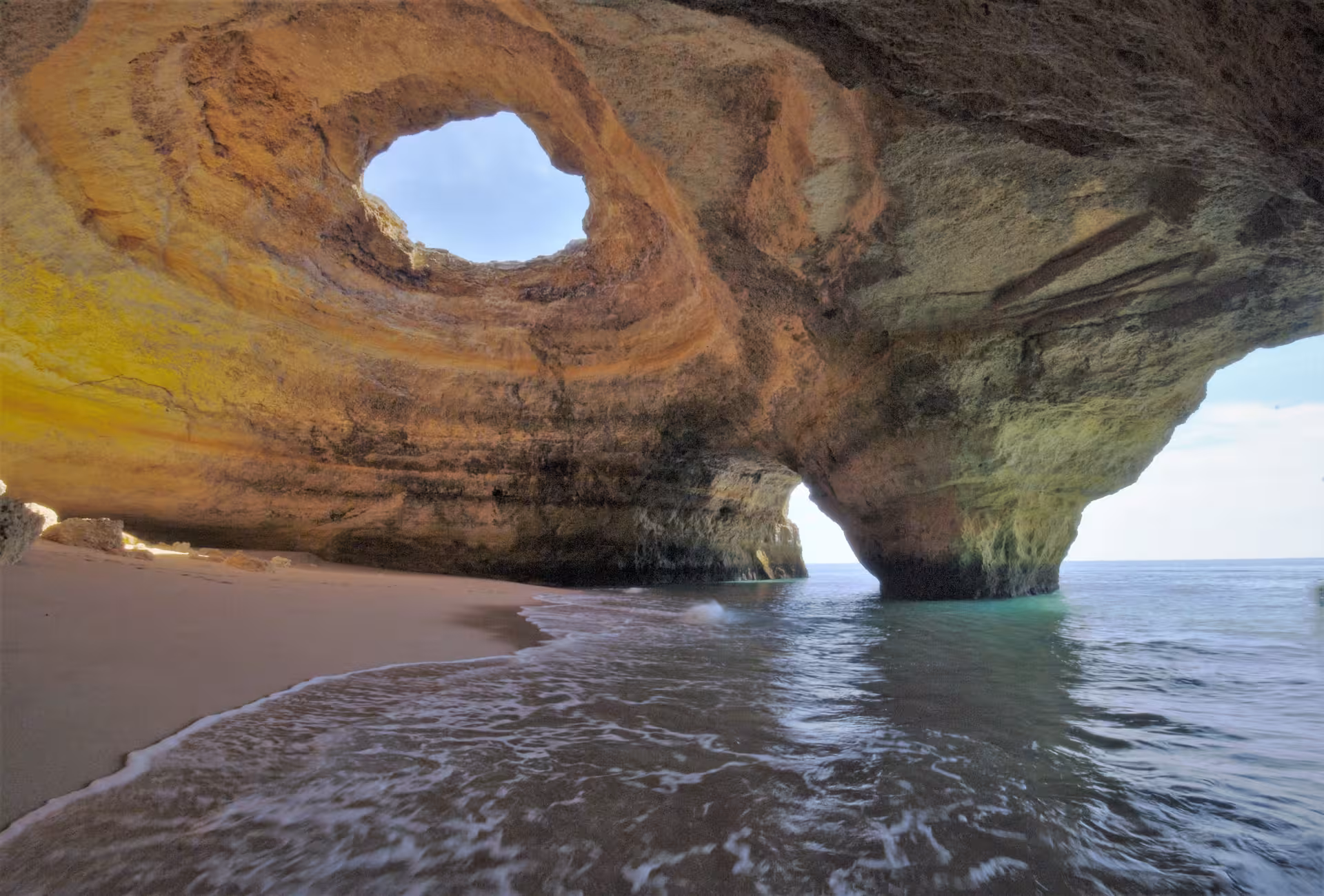 Hidden Algarve sea cave with golden cliffs, sandy beach and gentle Atlantic waves visited on a private sunset boat tour