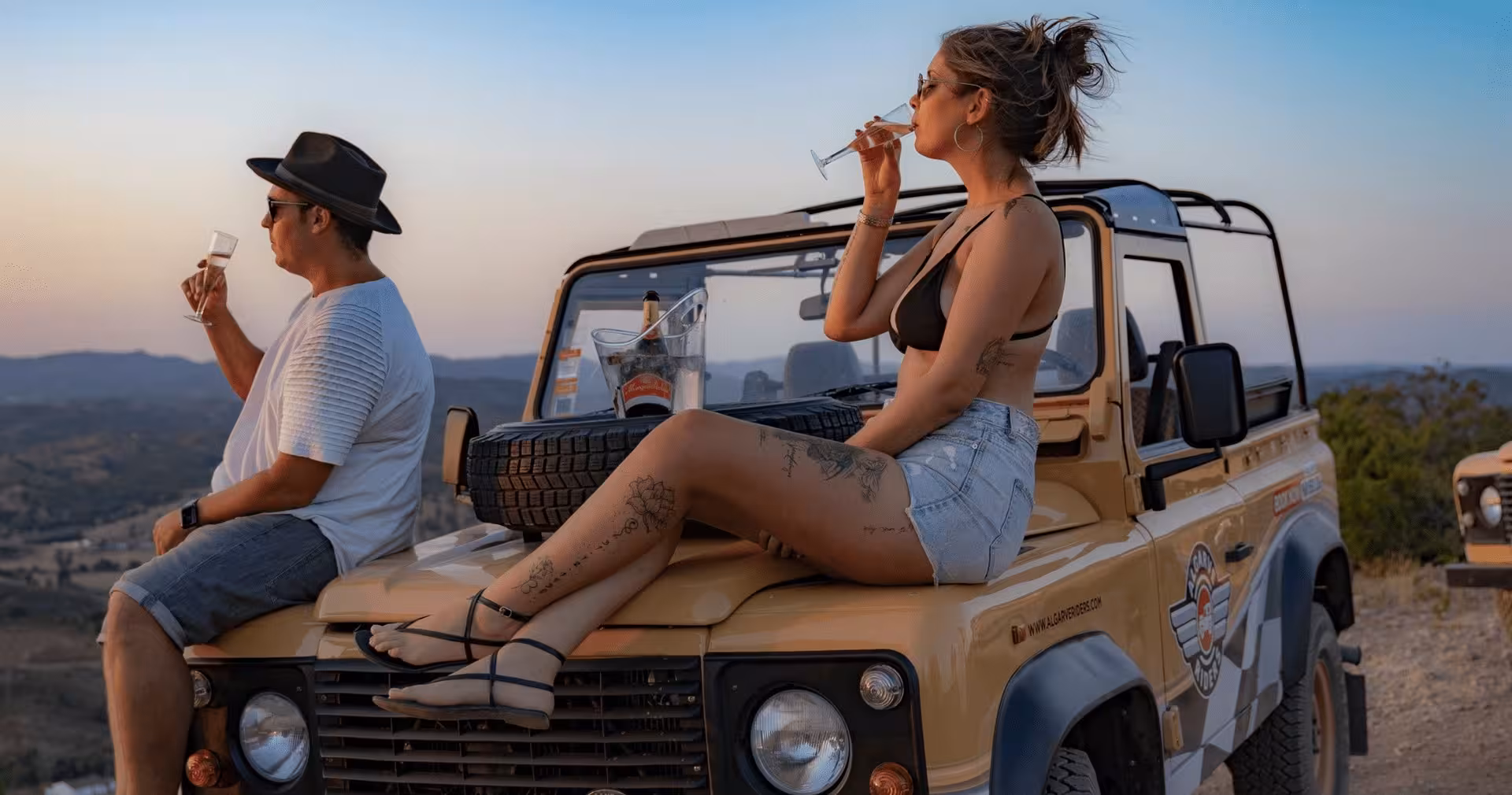 Couple relaxing on a jeep hood with champagne glasses enjoying a romantic Algarve private sunset safari tour