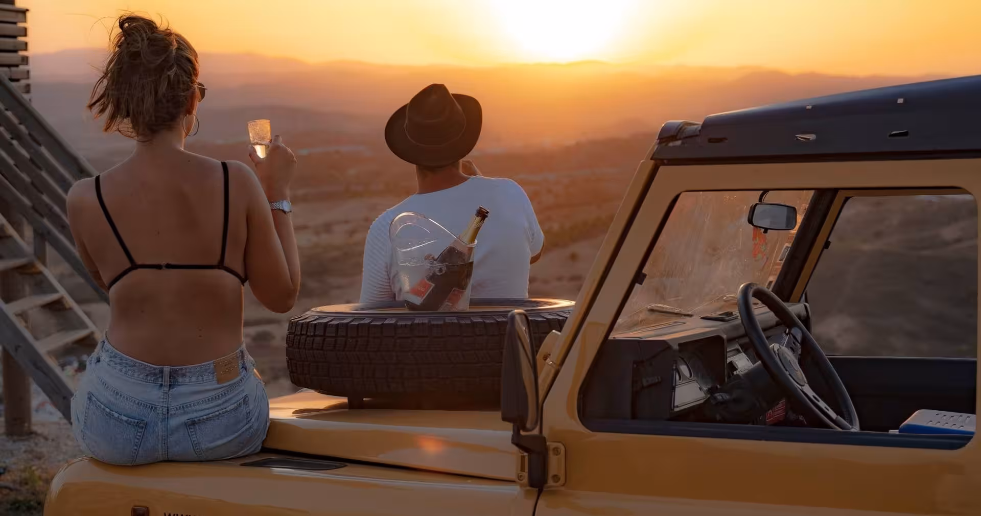 Romantic couple enjoying champagne beside a vintage jeep at breathtaking Algarve golden sunset