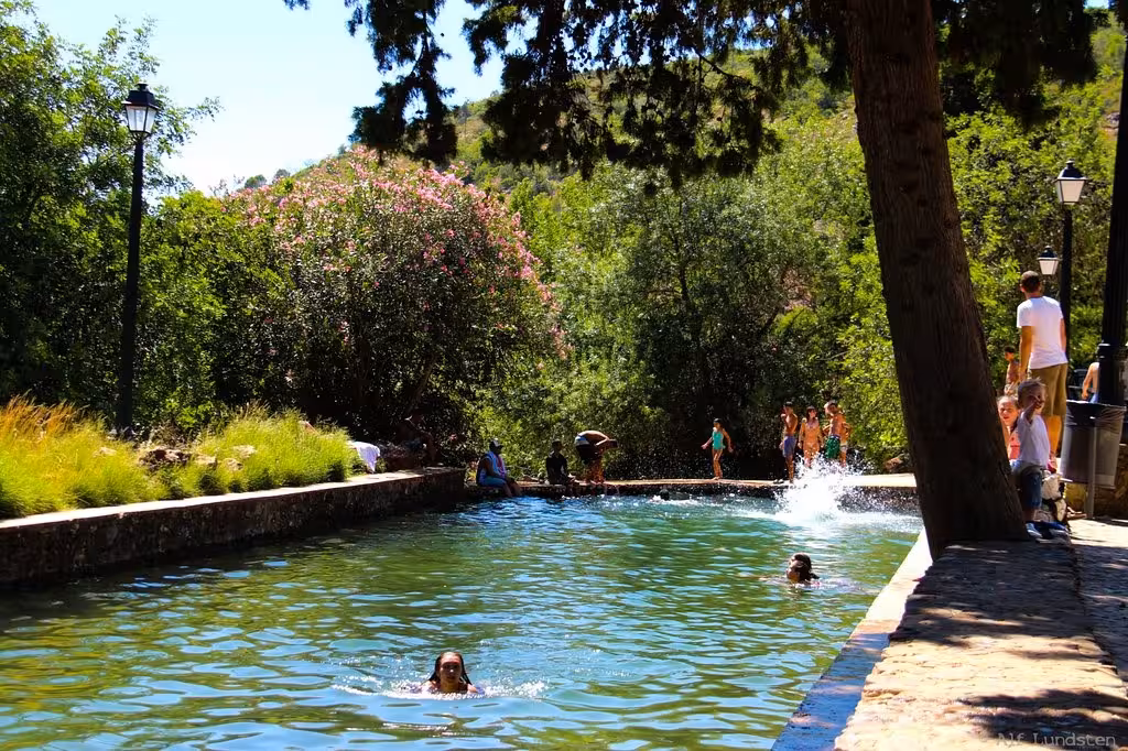 Families swim in a natural pool surrounded by lush trees during a sunny Algarve sunset tour with sparkling wine