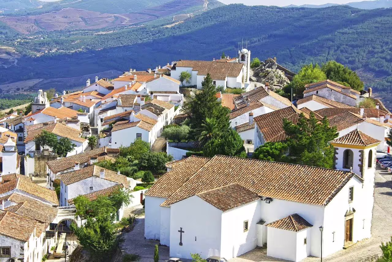 Scenic view of a charming village in the Algarve, showcasing traditional whitewashed houses and lush greenery under a clear sky.