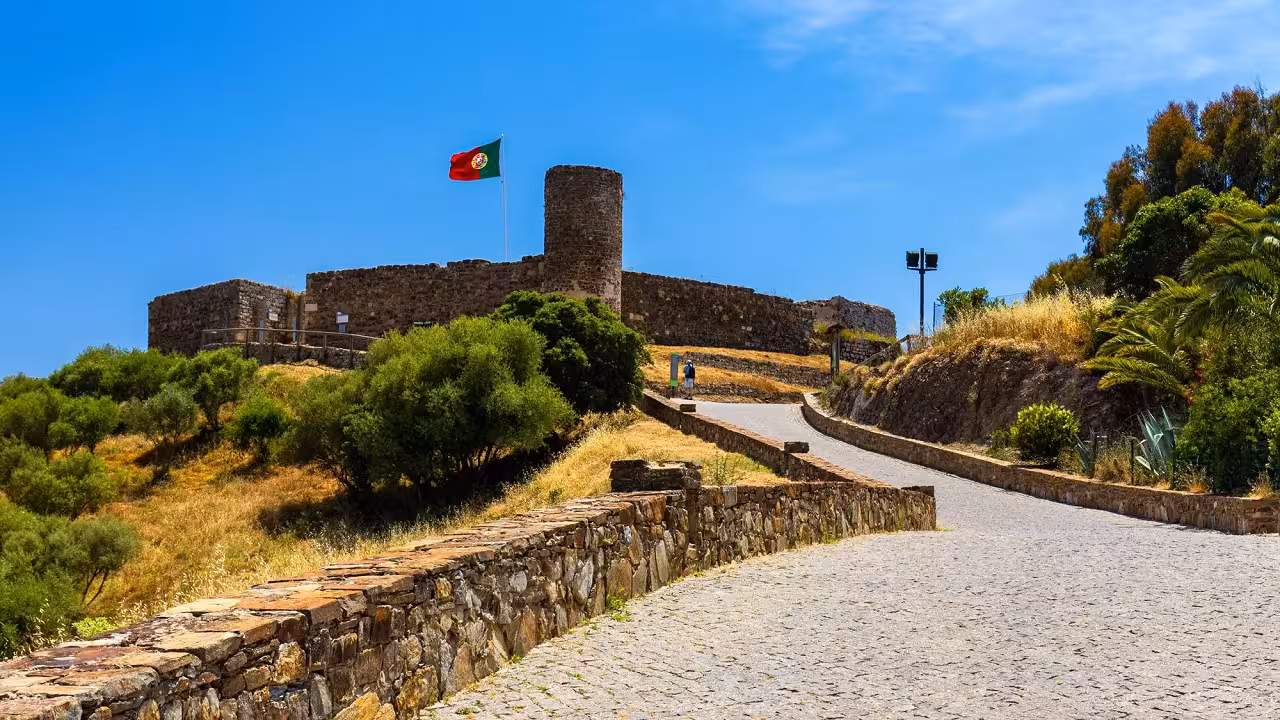 Historic Algarve hilltop fortress with Portuguese flag, cobbled path and coastal countryside views on West Coast full day tour