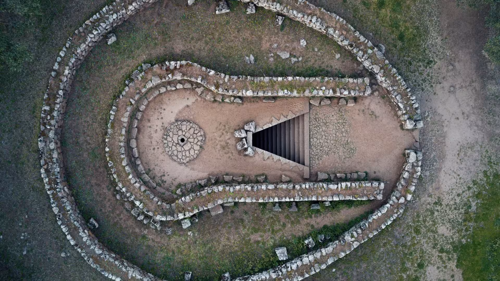 Discover Alghero's historic ruins from above, featuring stone structures and pathways surrounded by greenery.