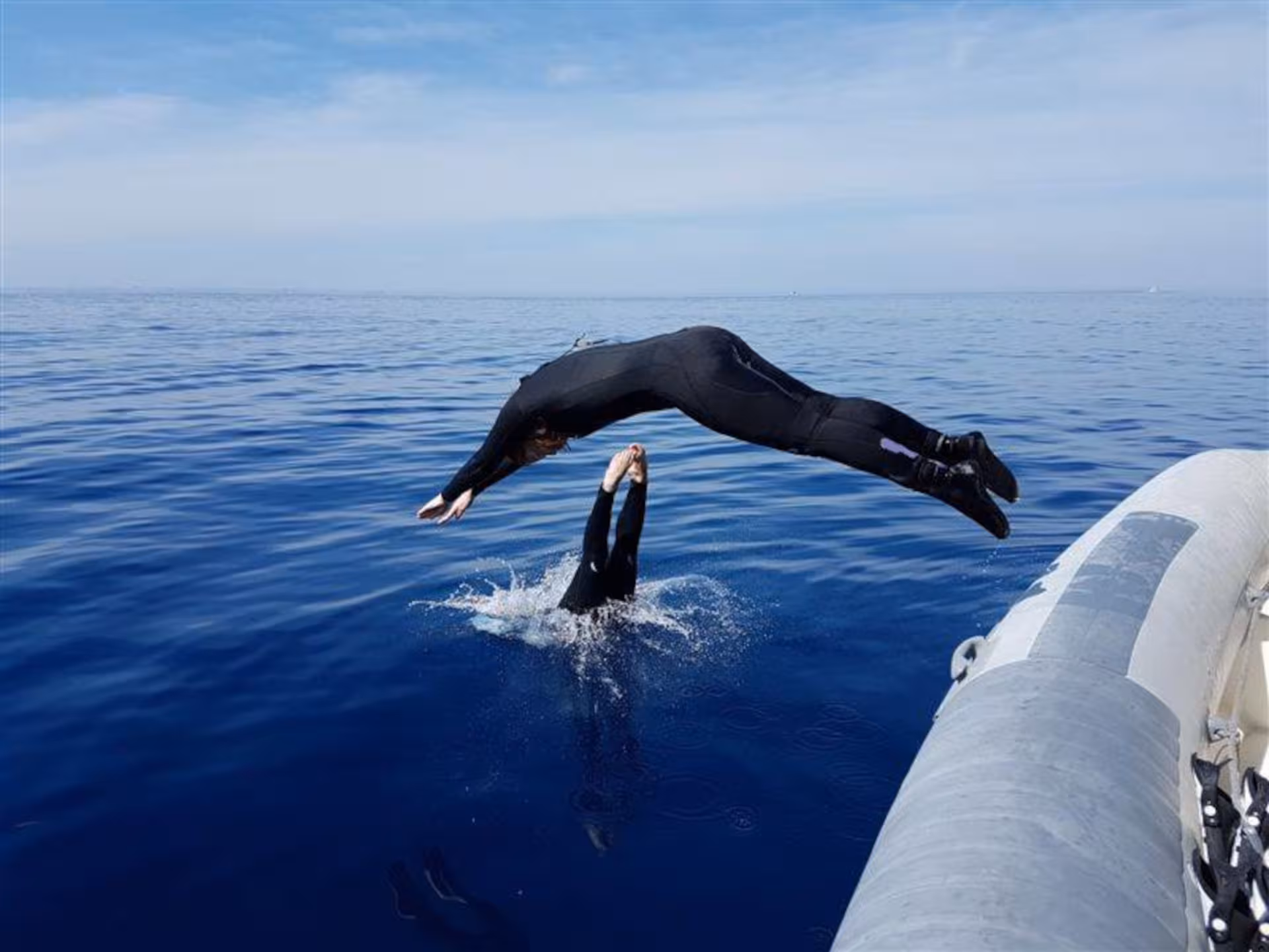 Diver gracefully backflips into the pristine waters of Capo Caccia from a boat during a professional dive in Alghero.