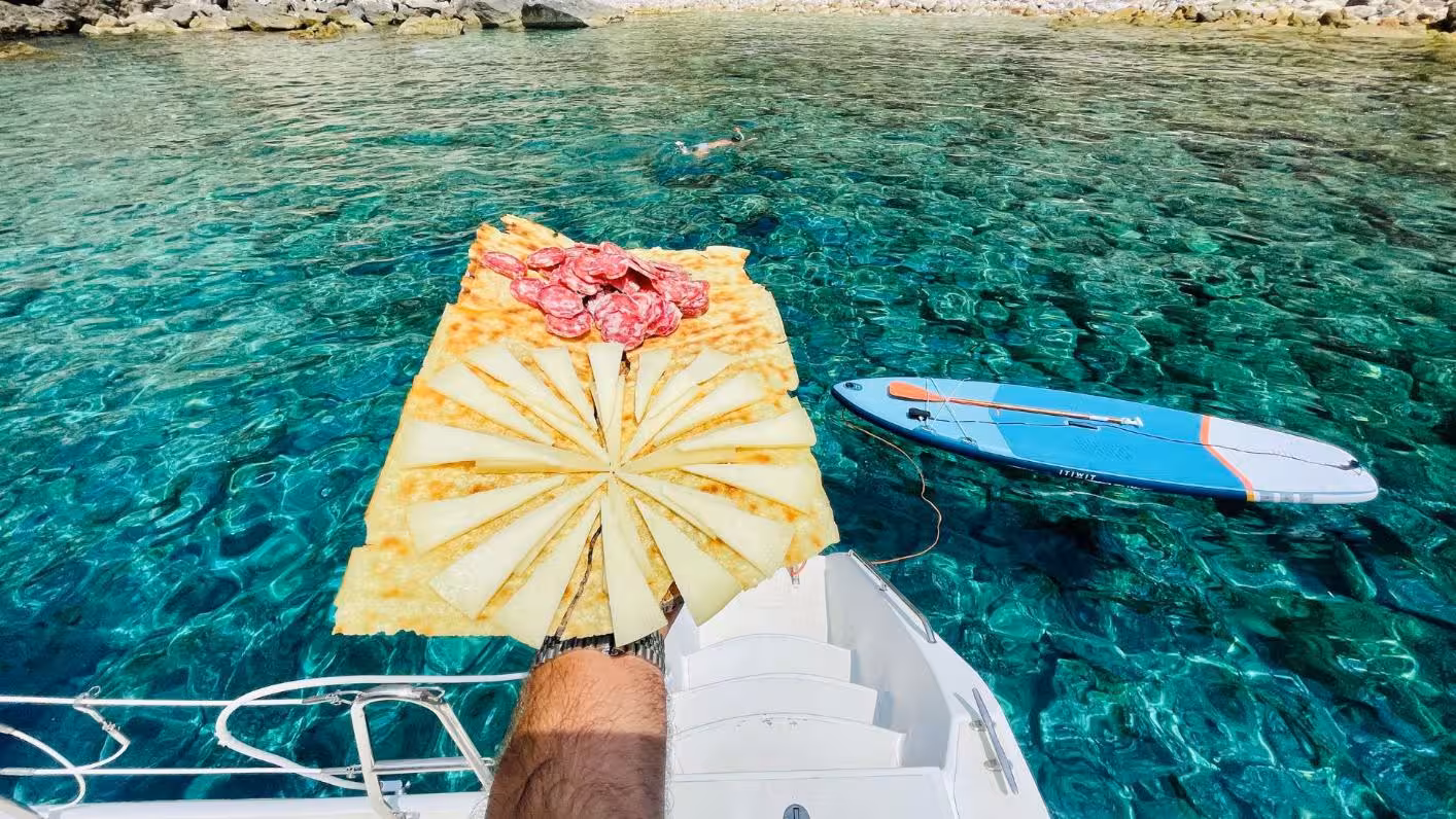 Enjoying a delicious cheese and salami platter on a catamaran in Porto Conte Park with paddleboard in the clear waters.
