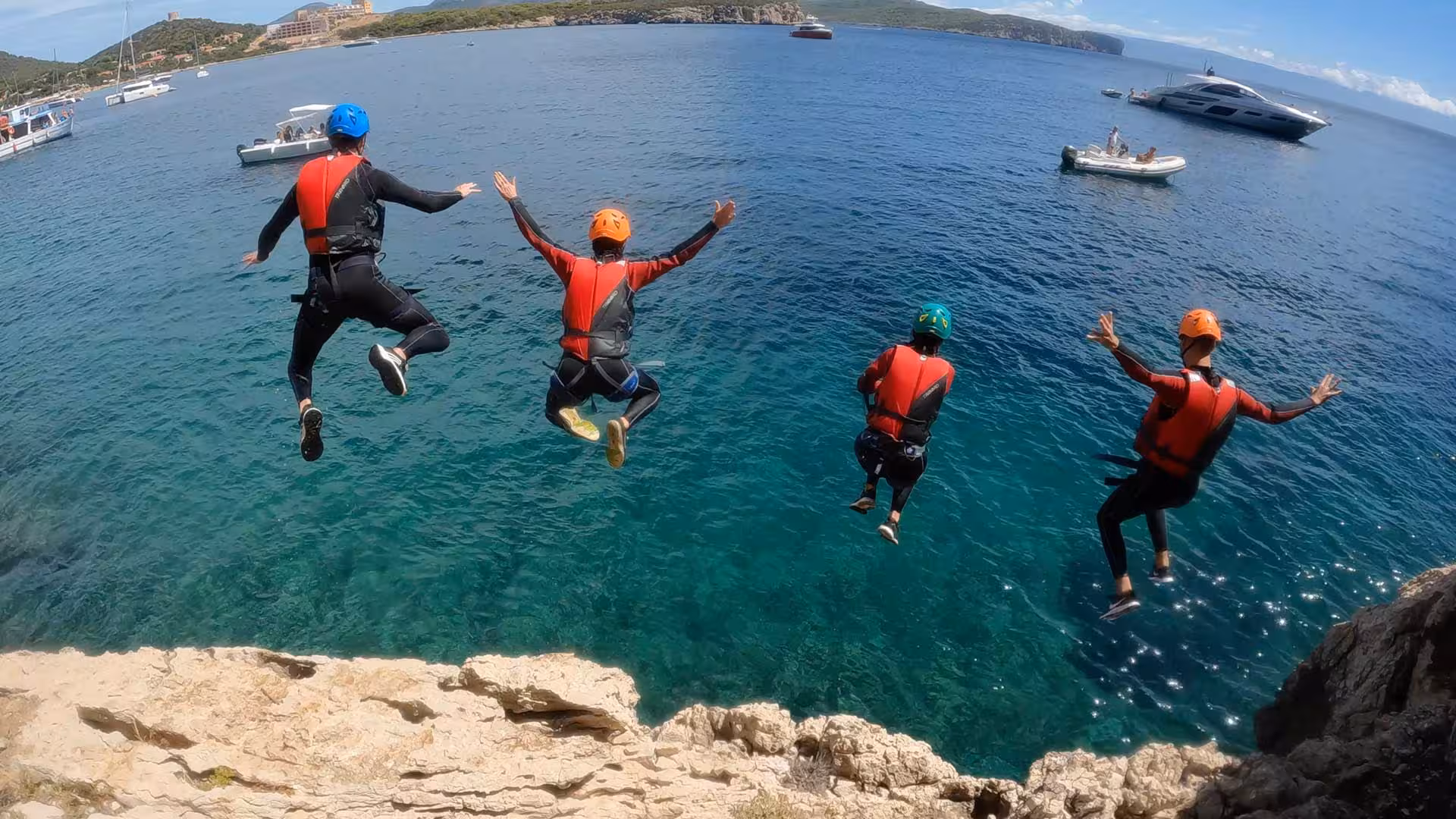 Group of thrill-seekers leaping off a cliff into clear waters at Cala Dragunara, Porto Conte Park, Alghero coasteering.