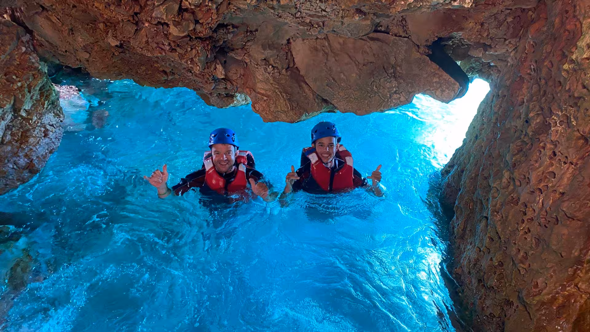 Adventurers coasteering through turquoise waters at Cala Dragunara, Alghero, wearing helmets and life jackets.