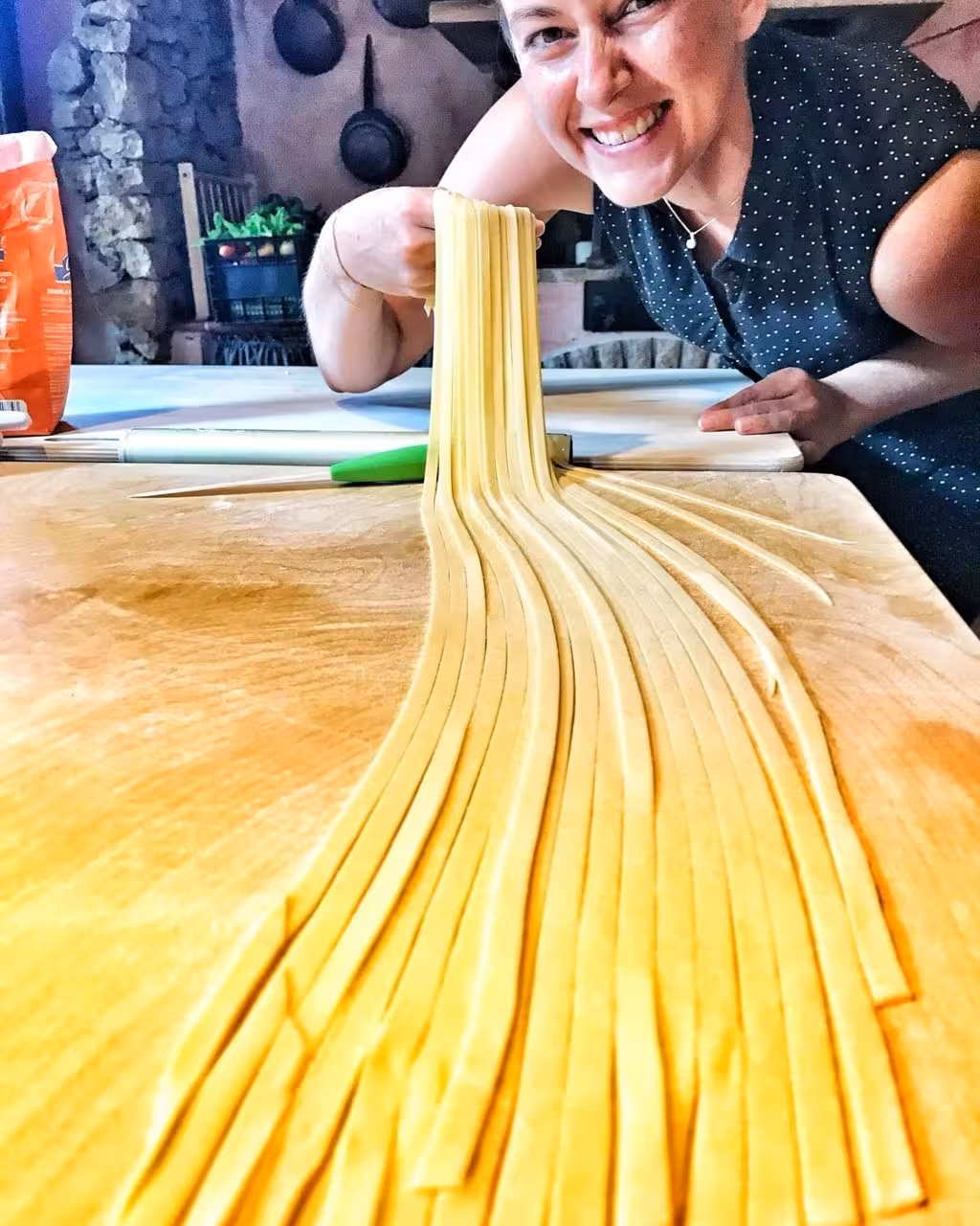 Smiling participant holding fresh fettuccine pasta during a hands-on cooking class in Olmedo, Alghero.