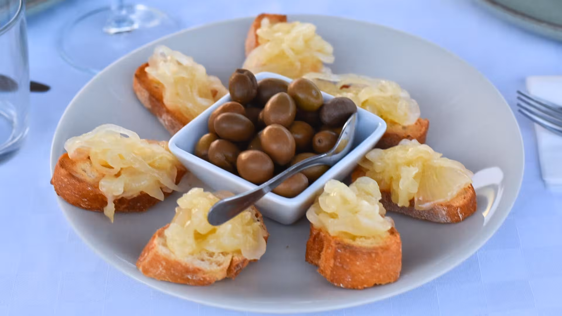 Plate of crostini with caramelized onions and olives, perfect for Alghero vineyard aperitif experience.