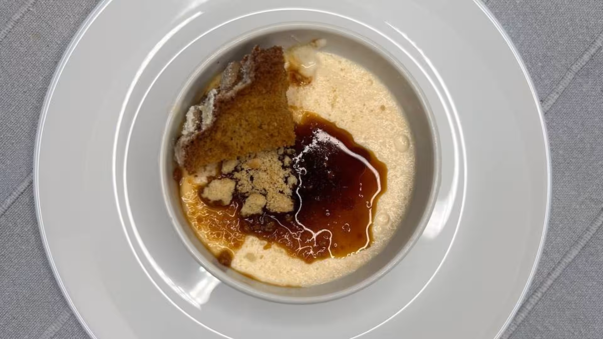 Delicious dessert served on a white plate, featuring creamy pudding with a caramel sauce and cake pieces in Alghero.