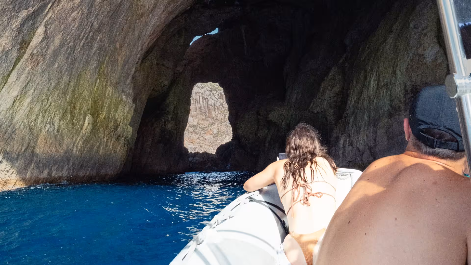 Tourists on a dinghy approaching a scenic cave entrance in Capo Caccia during Alghero snorkeling adventure.