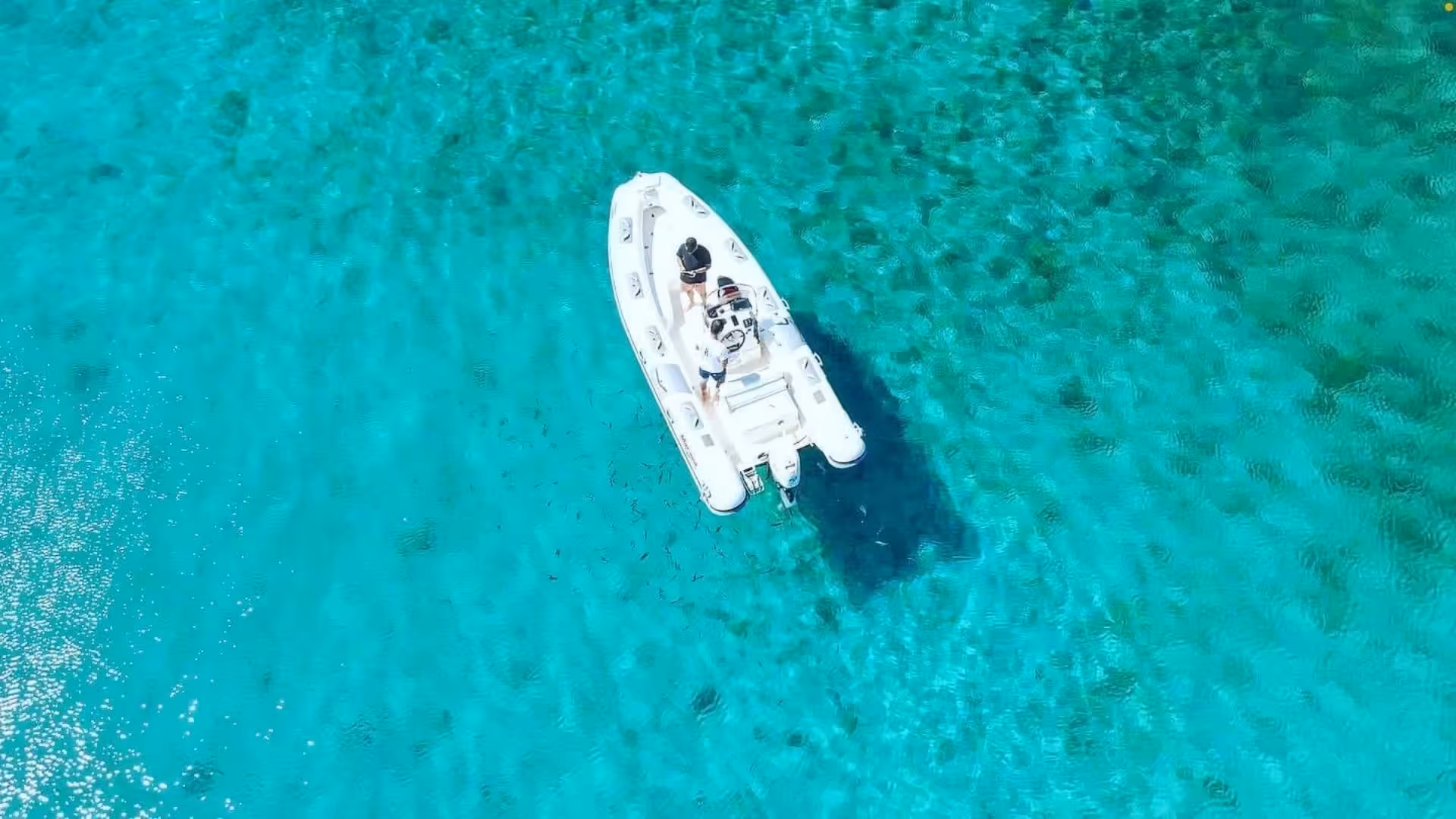 Aerial view of a dinghy cruising on the crystal-clear waters of Porto Conte, Alghero, ideal for snorkeling adventures.