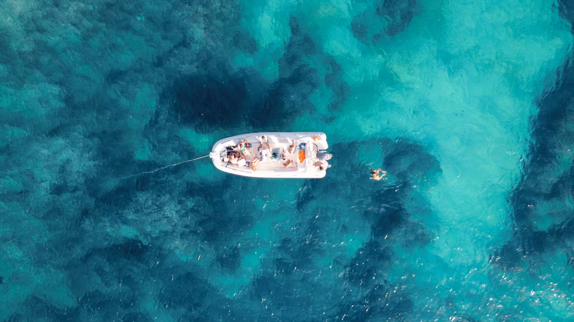Aerial view of a dinghy with tourists exploring turquoise waters during a snorkeling tour in Porto Conte, Alghero.