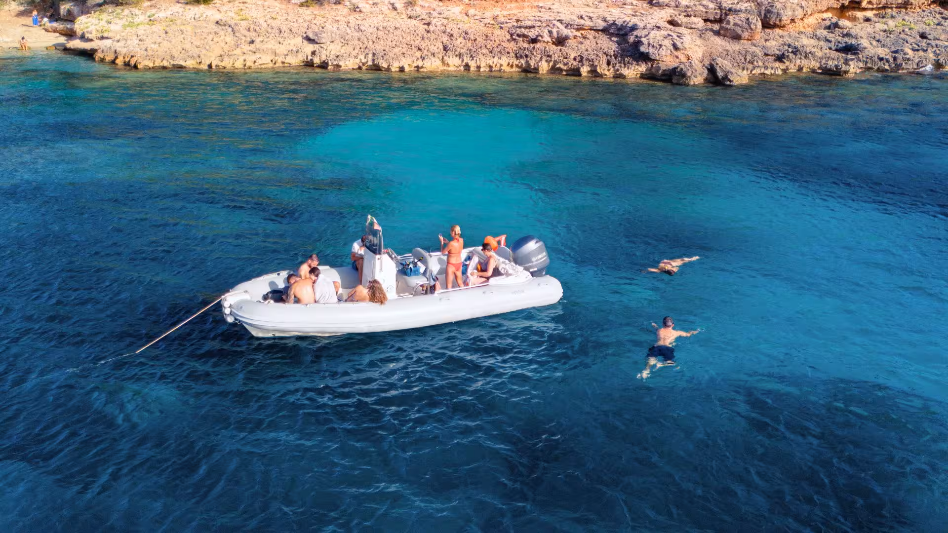 Dinghy with people snorkeling in the vibrant waters of Porto Conte, Alghero coastline in view.