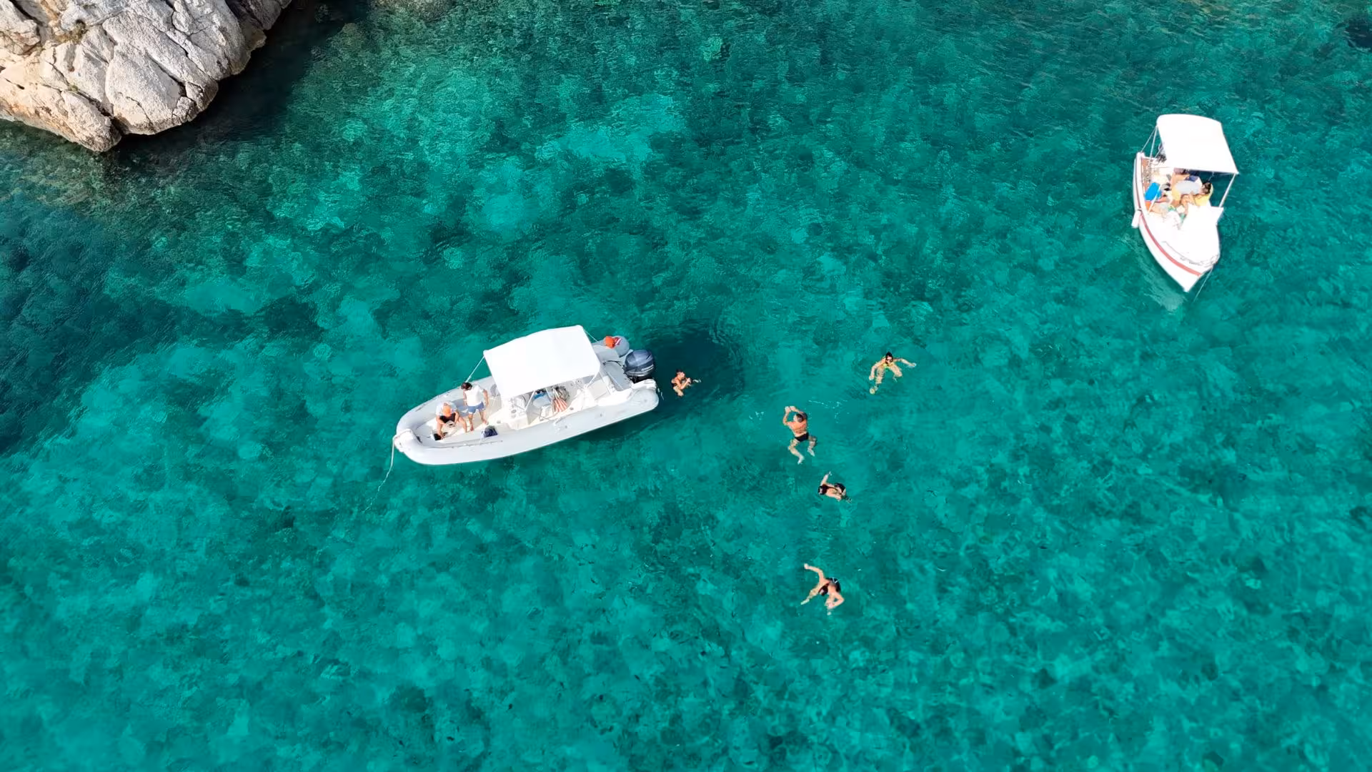 Aerial view of a dinghy tour with swimmers enjoying the crystal-clear waters of Capo Caccia in Alghero.