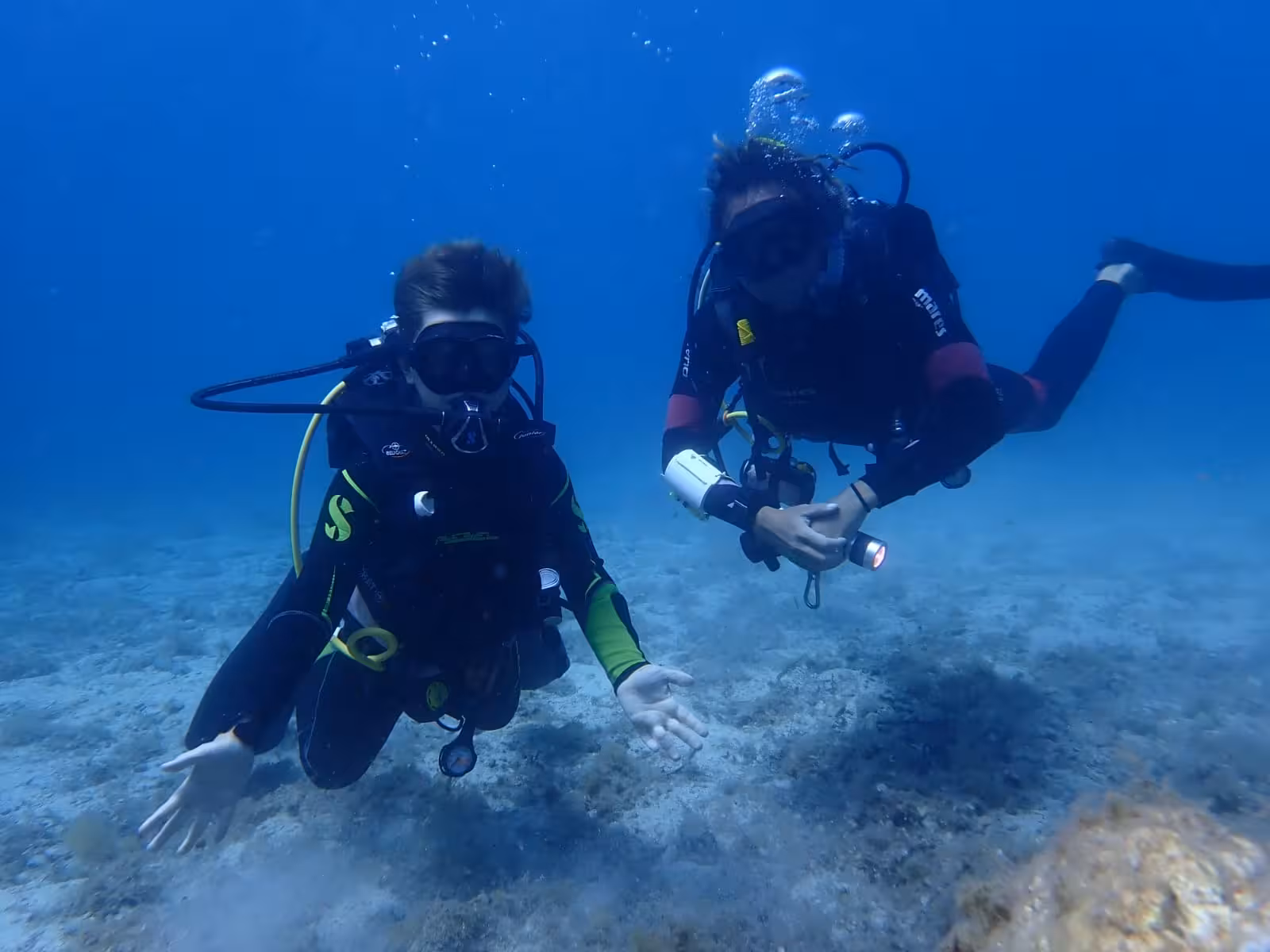 Two divers explore the clear blue waters of Alghero, showcasing the excitement of a diving baptism experience.