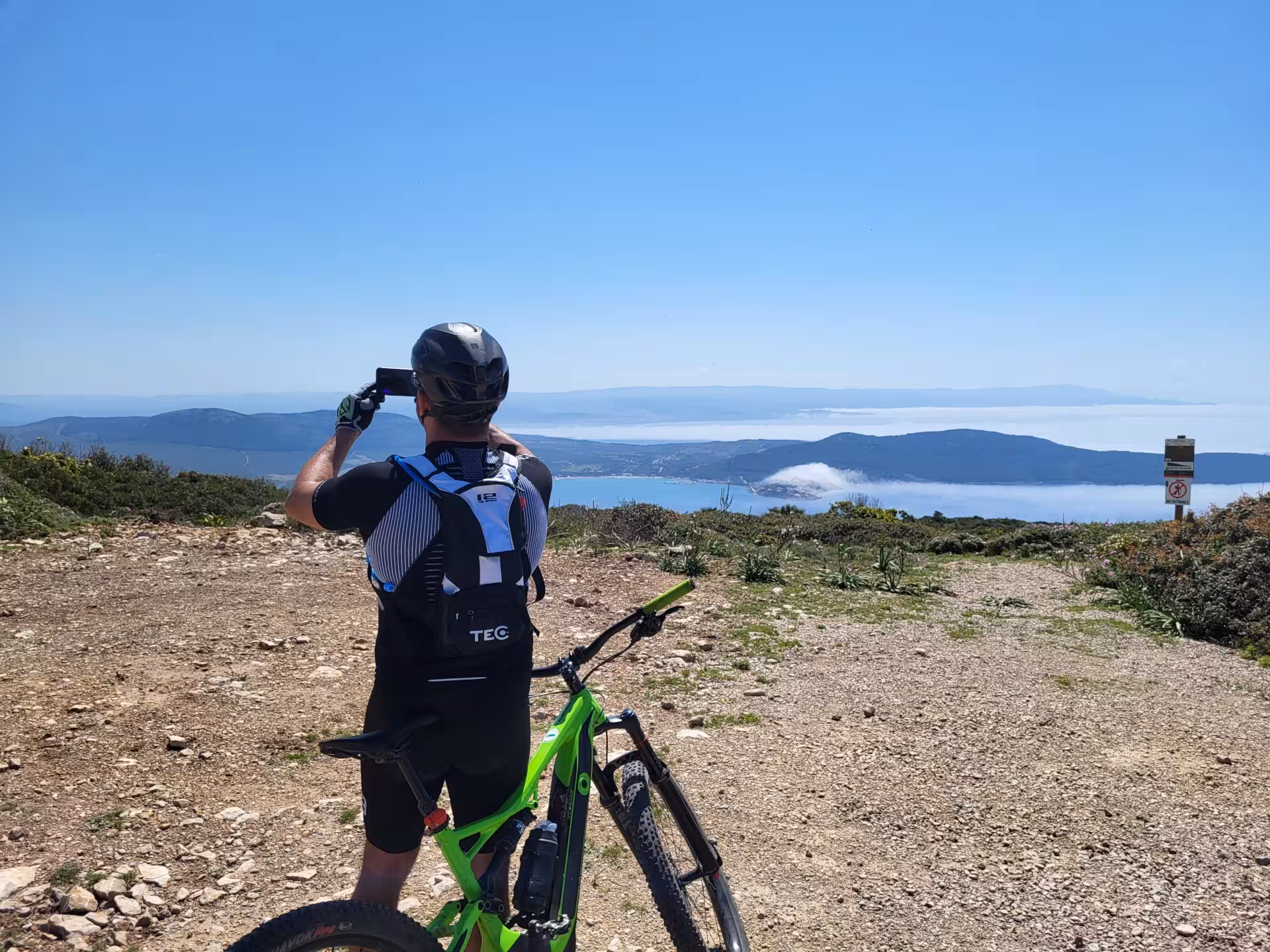 Cyclist photographing scenic views during Alghero e-bike tour in Porto Conte Park.
