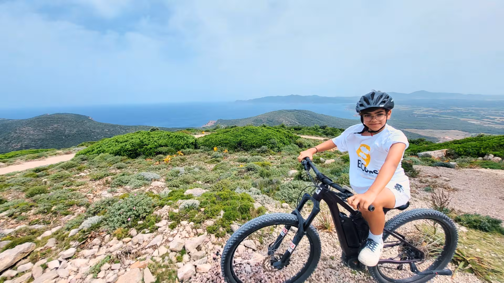 Cyclist enjoys stunning sea views on an Alghero e-bike tour in Porto Conte Park amidst vibrant green landscapes.