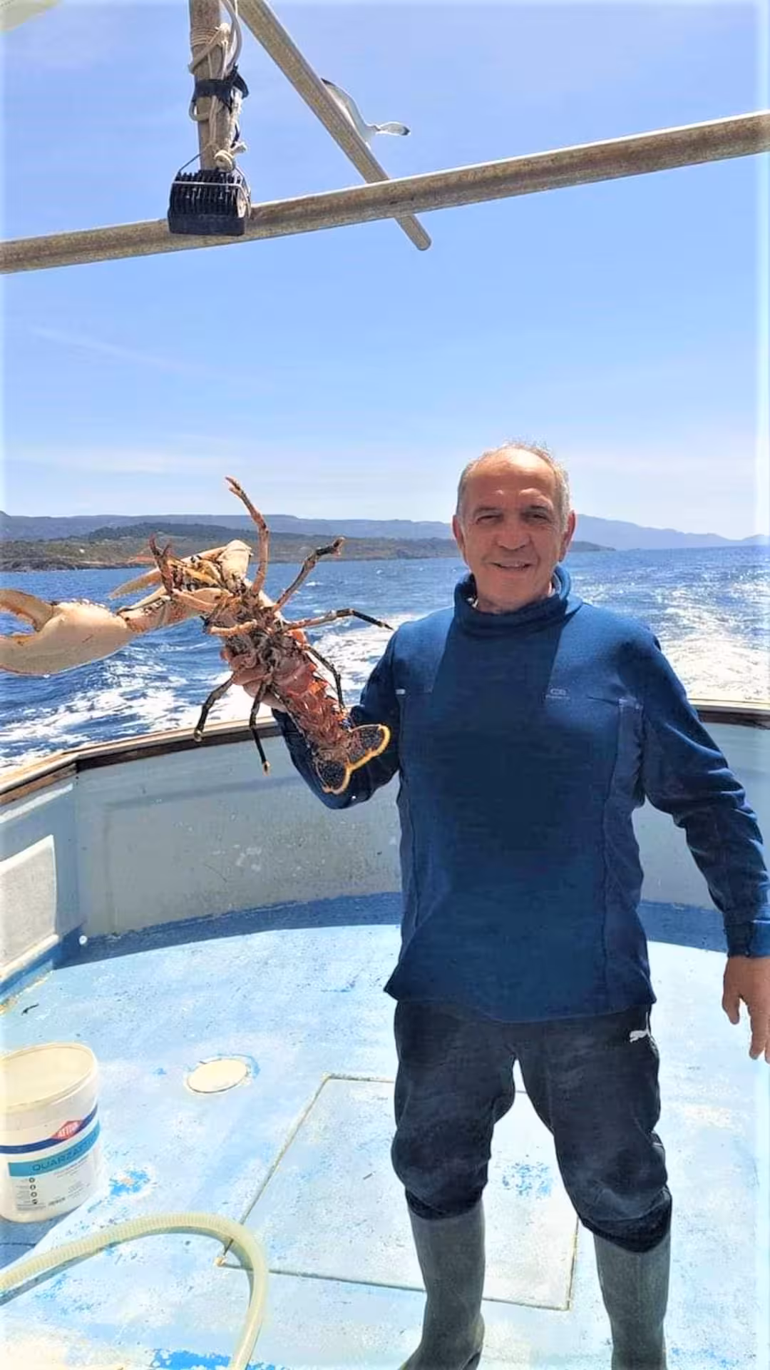 Proud fisherman displays a large lobster on deck during an Alghero fishing tour in the Capo Caccia marine area.