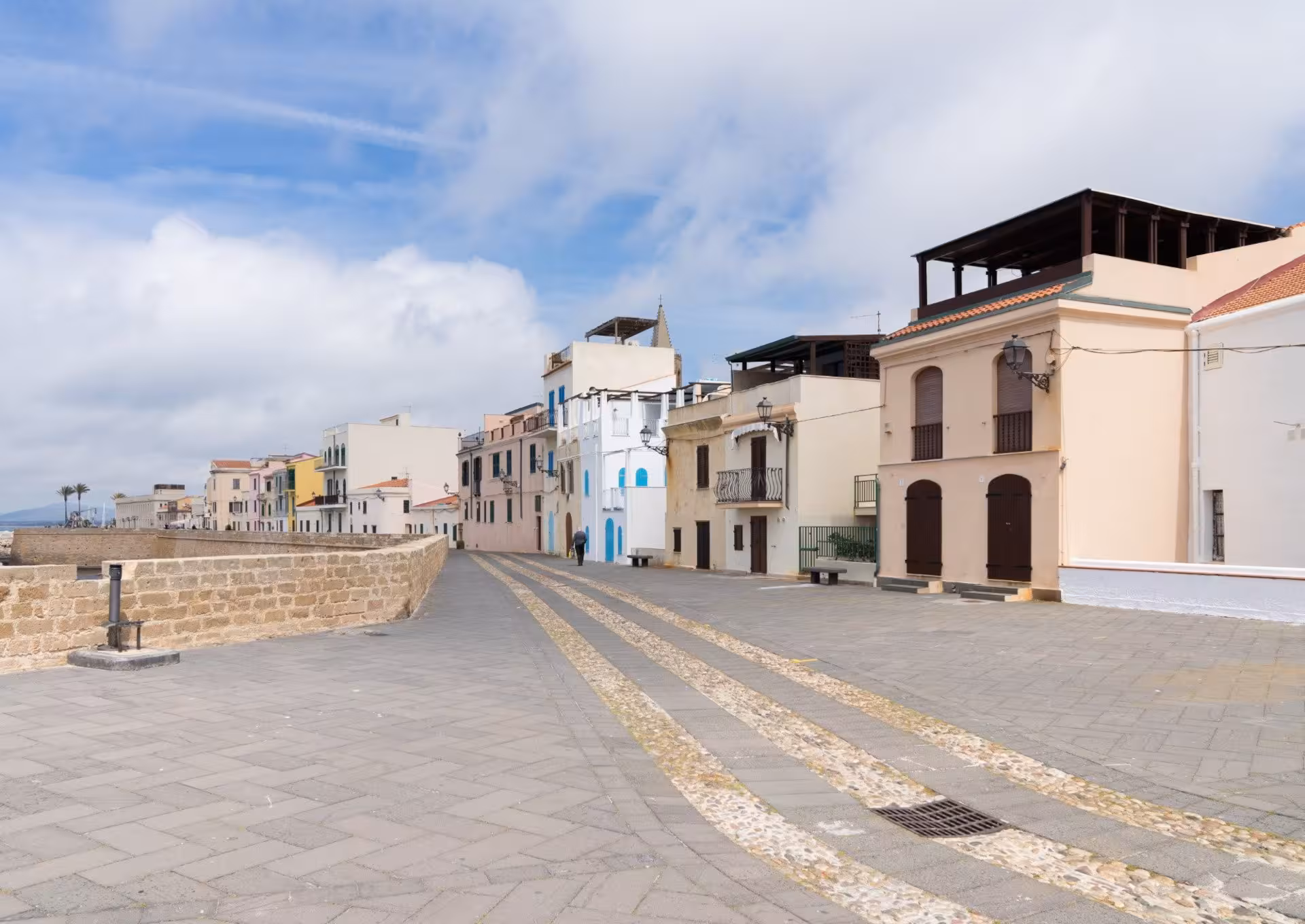 Charming cobblestone street in Alghero's historic centre lined with colorful buildings and blue sky.