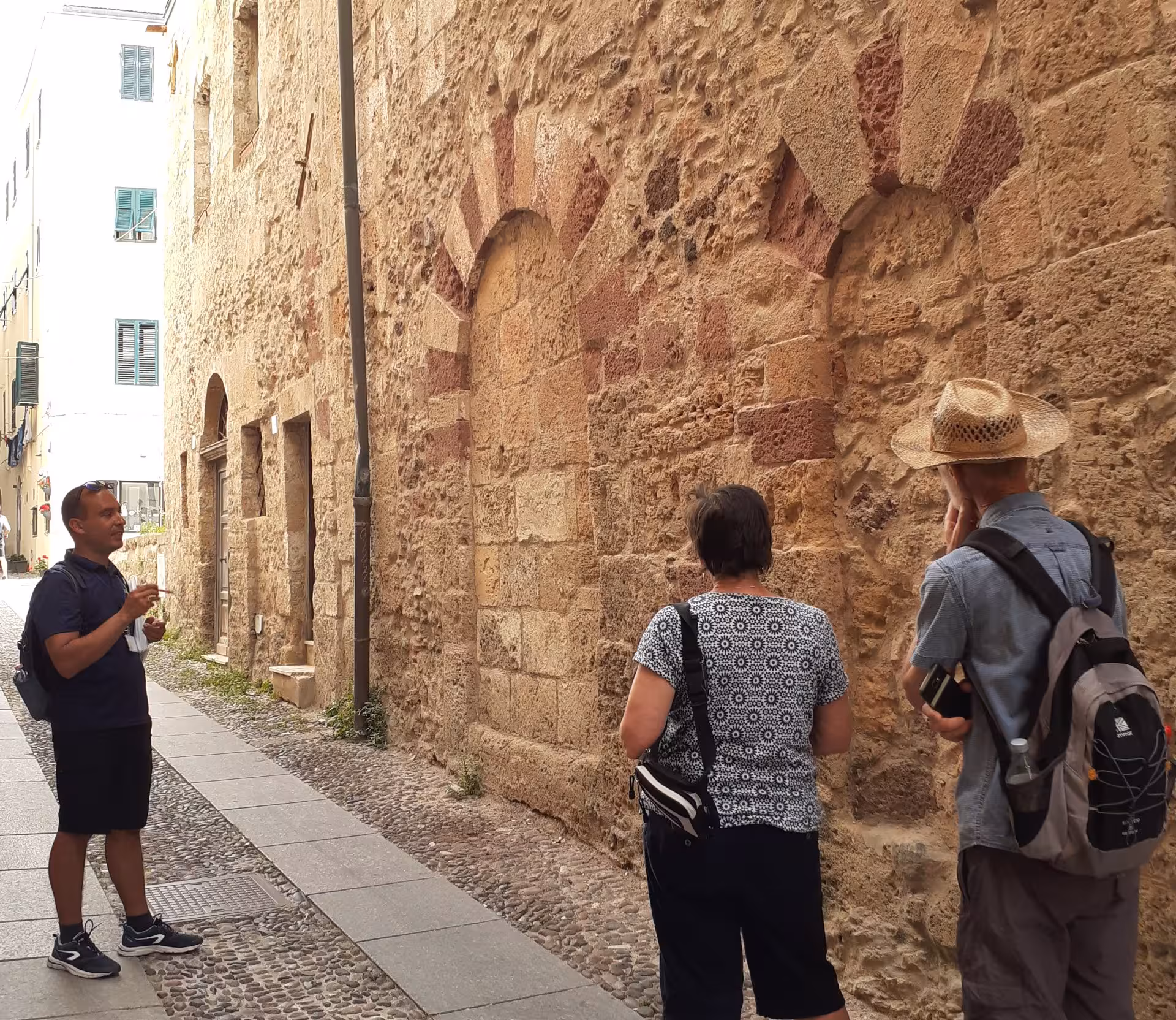 Tour guide explains Alghero's ancient walls to visitors on a historic center walking tour.