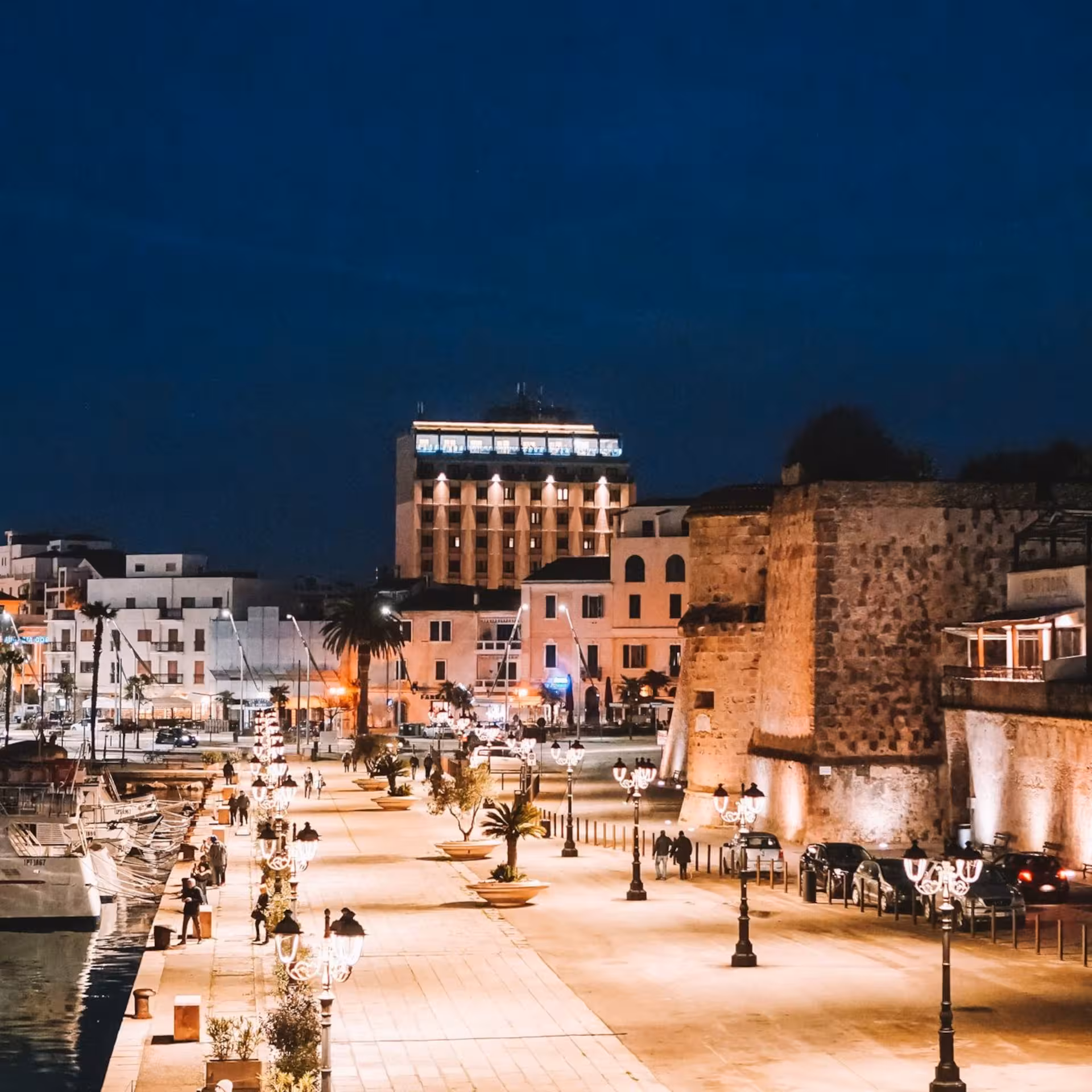 Alghero's illuminated waterfront and historic buildings at night, perfect for a scenic evening guided tour.