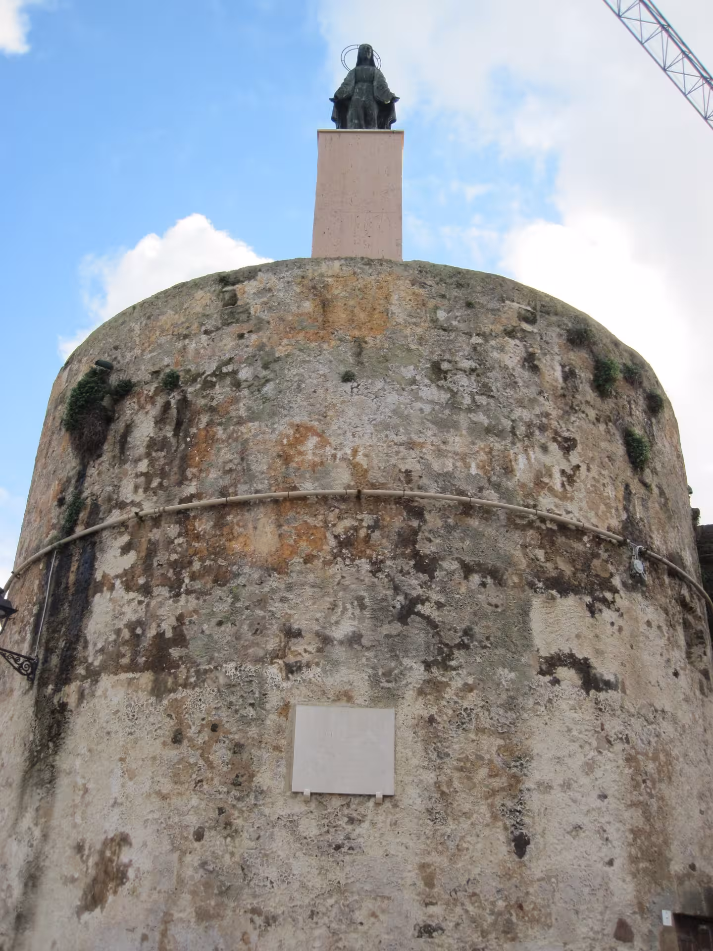 Historic Alghero tower with a statue on top under a bright blue sky, perfect for cultural guided tours.