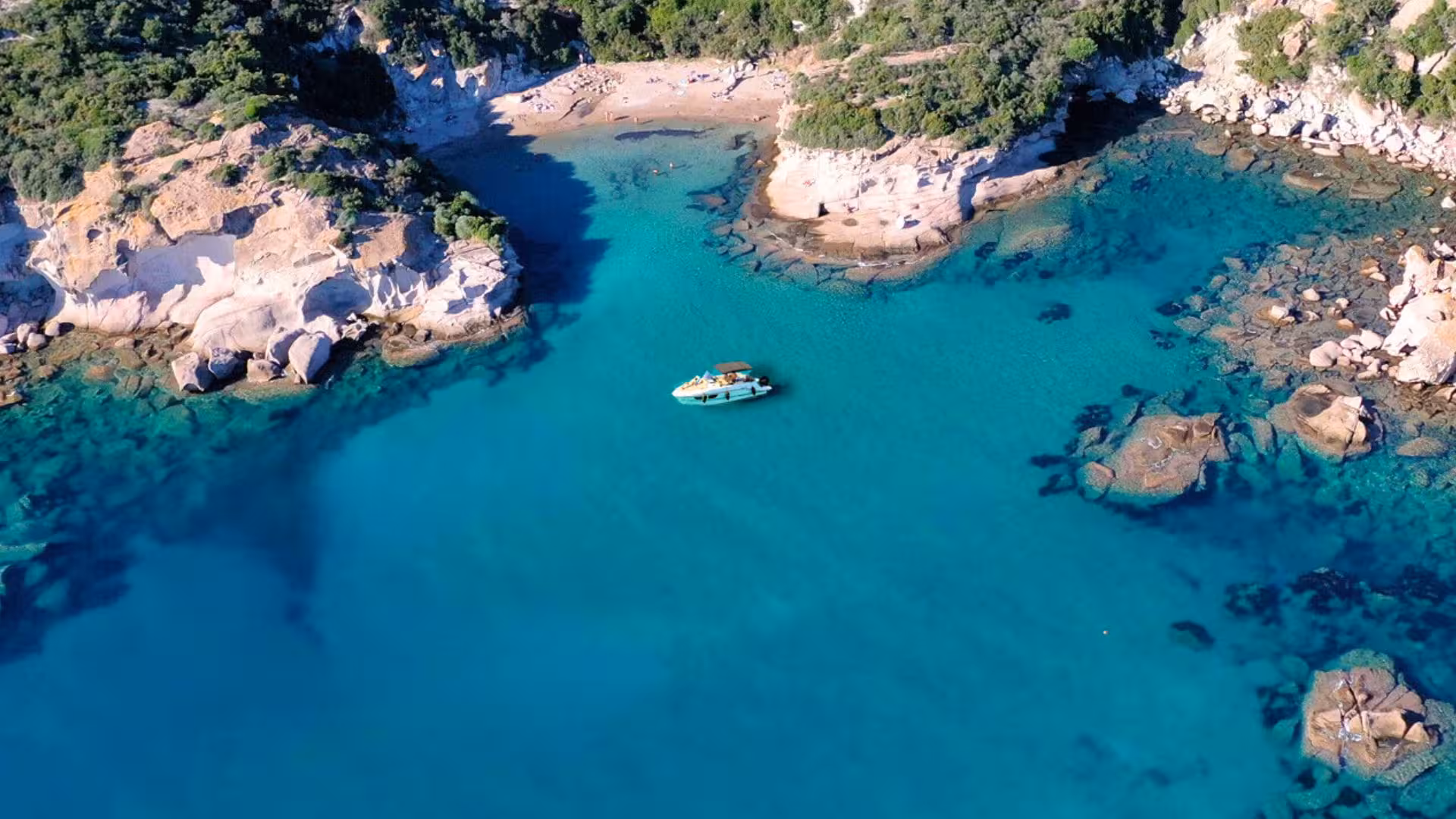 Aerial view of a motorboat on crystal-clear waters surrounded by rocky coastline on a half-day trip from Alghero.