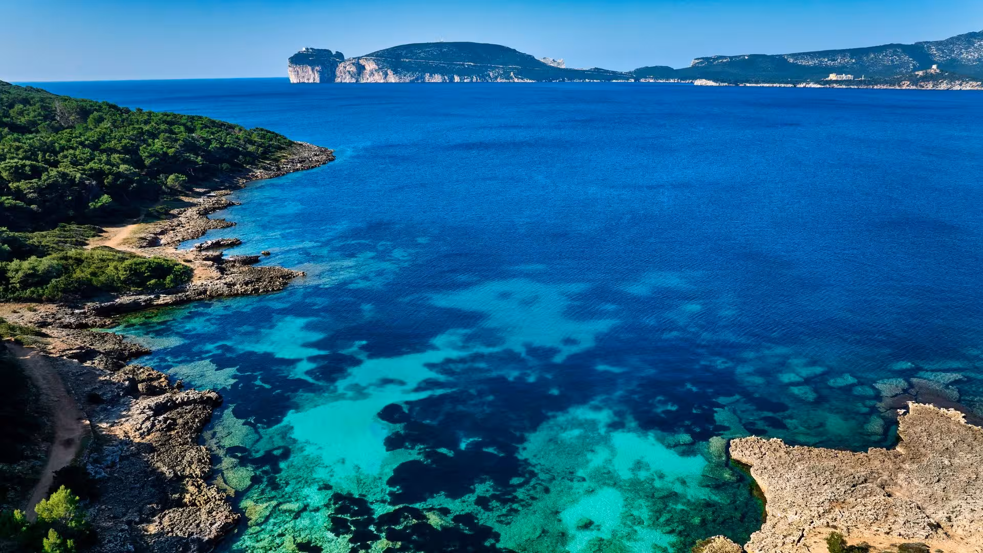 Aerial view of Porto Conte park's turquoise waters and rugged coastline in Alghero, perfect for trekking adventures.