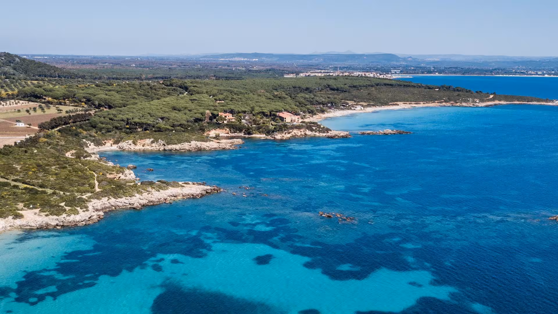 Scenic aerial view of Porto Conte's coastline, lush greenery meeting pristine blue waters, perfect for snorkeling tours.