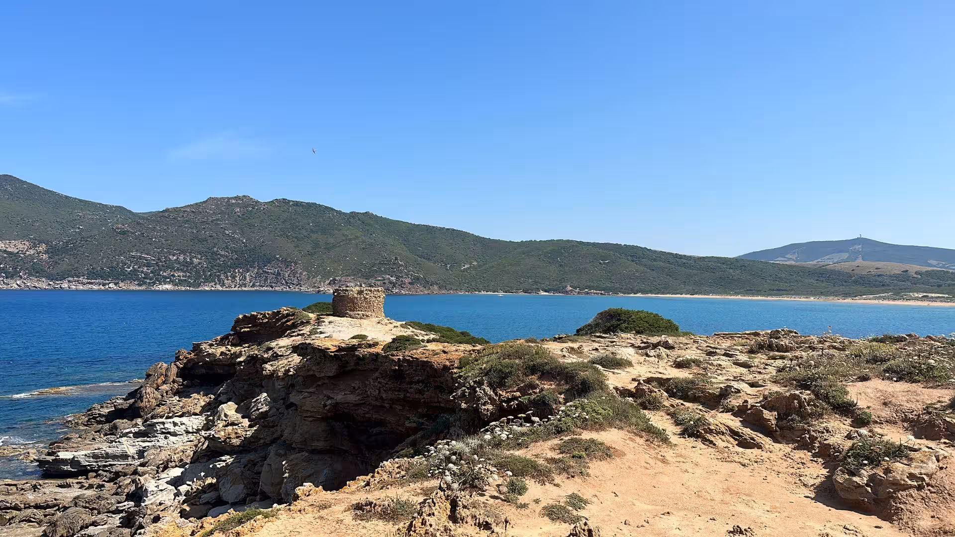 Scenic coastal view of Alghero with ancient watchtower and lush hills, perfect for exploring on a quad tour.